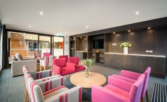 a hotel lobby with a pink and gray couch , chairs , and a round table in the center at Quest Wodonga