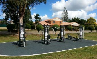 a group of outdoor exercise equipment is set up in a park , with trees and buildings visible in the background at Quality Hotel Robertson Gardens