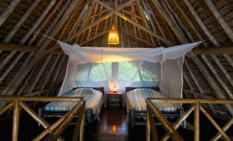 a cozy bedroom with wooden walls , thatched roof , and mosquito nets , giving it a warm and inviting atmosphere at Lazy Lagoon