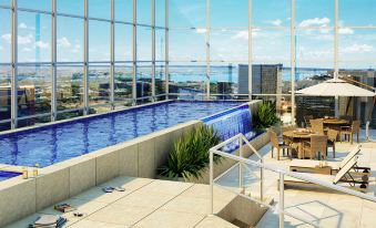 a rooftop pool surrounded by glass walls , with lounge chairs and umbrellas placed around it at Hplus Vision Executive