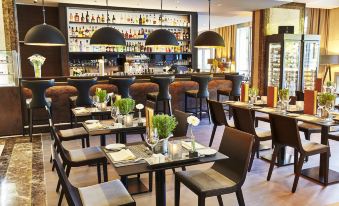 a restaurant with multiple tables and chairs , some of which have floral arrangements on them at Steigenberger Hotel Koln