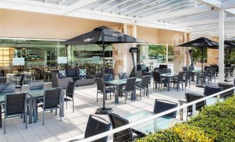 an outdoor dining area with multiple tables and chairs , some of which are covered by umbrellas at Pelican Waters Resort