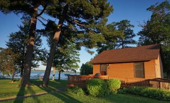 a wooden house with a red roof , surrounded by trees and grass , near a body of water at Sugar Lake Lodge