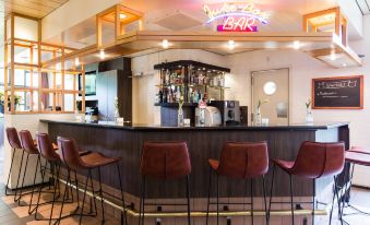 a modern bar with wooden furniture , a counter filled with liquor bottles , and an orange neon sign above it at Bastion Hotel Bussum Hilversum