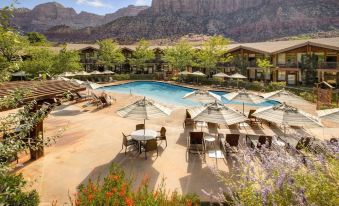 a resort with a large pool surrounded by lounge chairs , umbrellas , and flowers in front of a mountain at Desert Pearl Inn