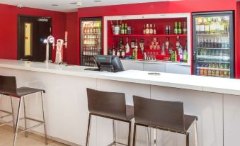 a bar with a white counter and two chairs , featuring a variety of bottles and glasses at Travelodge Maidenhead Central