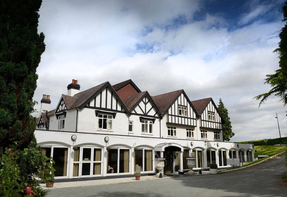 a large , white building with a brown roof and brown trim is surrounded by trees and bushes at Buckatree Hall Hotel