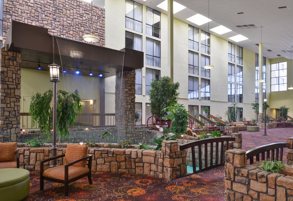 a large hotel lobby with a stone wall , a staircase , and a potted plant in the corner at Ramada Plaza by Wyndham Sheridan Hotel & Convention Center