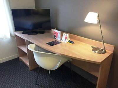 a wooden desk with a chair and lamp , next to a tv on the wall at Ibis Melbourne Hotel and Apartments