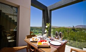 a table set with plates , glasses , and a vase on a balcony overlooking the countryside at El Plantío Golf Resort