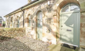 a stone building with a green door , surrounded by gravel and plants , under the sun at Kennels