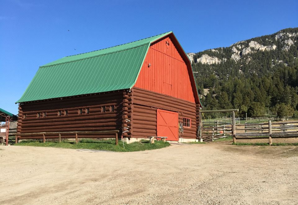 a large wooden barn with a green roof , situated in a rural setting surrounded by trees and mountains at Diamond J Ranch