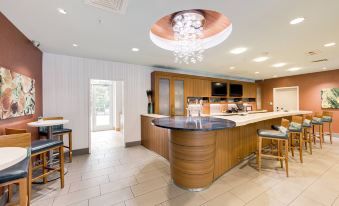 a modern kitchen with wooden cabinets and a curved countertop features a chandelier hanging from the ceiling at SpringHill Suites Houston the Woodlands