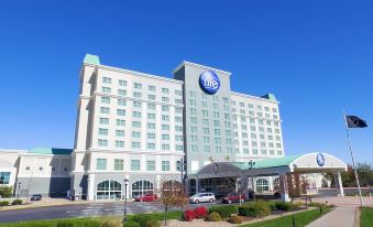 a large white hotel with a blue sign on the front , surrounded by trees and cars at Isle Casino Hotel Waterloo