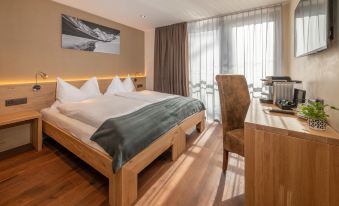 a modern hotel room with wooden flooring , large windows , and a bed dressed in white bedding at Hotel Heimatlodge