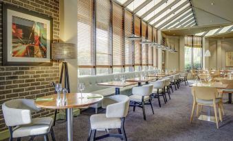a modern restaurant with large windows , wooden tables and chairs , and artwork on the walls at DoubleTree by Hilton Manchester Airport