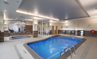 an indoor swimming pool with a large rectangular shape , surrounded by modern amenities such as lounge chairs and tables at Fairfield by Marriott Edmonton International Airport