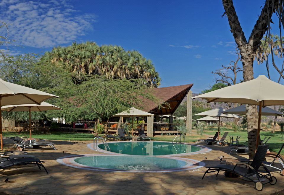 a resort with a large outdoor pool surrounded by lounge chairs and umbrellas , providing a relaxing atmosphere for guests at Ashnil Samburu Camp