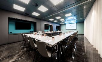 a long conference table with chairs and a large screen in the background , ready for a meeting at NH Collection Antwerp Centre