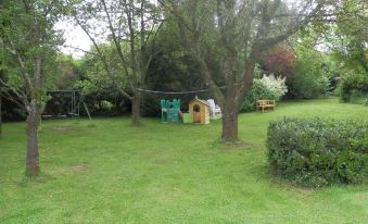a grassy yard with a swing set and a slide , surrounded by trees and bushes at La Cure