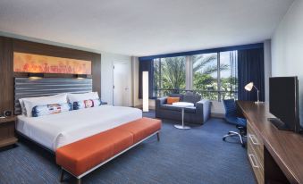 a large bed with an orange headboard is in a hotel room next to a desk and chair at Aloft Miami Dadeland