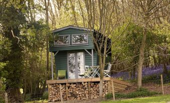 a small wooden house surrounded by trees and a wooded area , with a deck in front of it at Extraordinary Huts Ltd