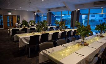 a well - lit banquet hall with multiple tables set for dining , each table having its own arrangement of flowers and candles at Garden Hotel