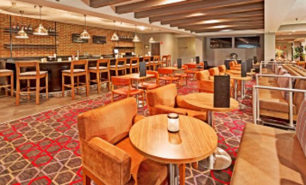 a modern lounge area with wooden tables and chairs , along with other furniture and decorations at Wyndham Garden Pittsburgh Airport