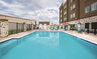 a large outdoor swimming pool surrounded by multiple buildings , with lounge chairs and umbrellas placed around the pool area at La Quinta Inn & Suites by Wyndham Houston Humble Atascocita