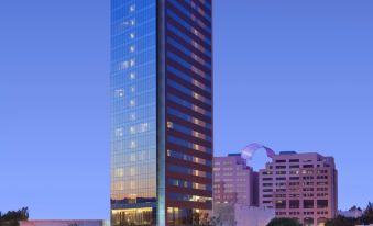 a tall , modern building with a blue glass facade is surrounded by trees and bushes at The Westin Guadalajara