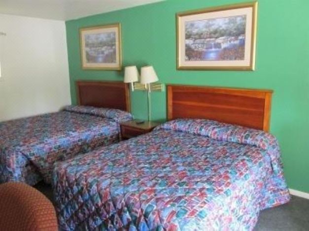a hotel room with two beds , each topped with floral bedspreads and matching pillows , surrounded by green walls and wooden headboards at Village Inn