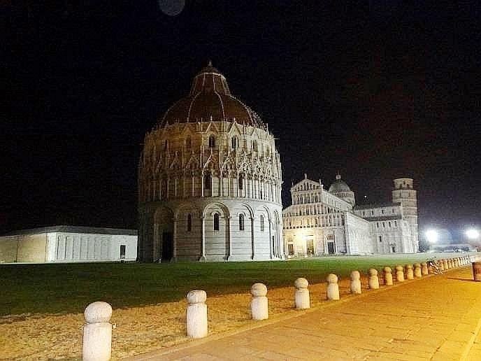 a nighttime scene of a large , circular building with a dome and multiple windows , surrounded by a grassy field at Hotel Leonardo