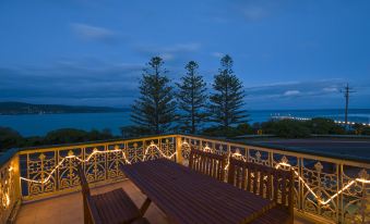 a wooden deck with a dining table and chairs , surrounded by palm trees and overlooking a body of water at Grand Pacific Hotel