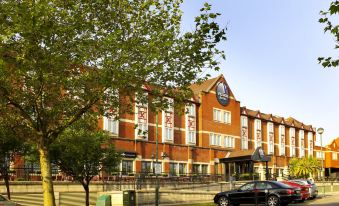 a brick building with a large sign on the front , surrounded by trees and parked cars at Village Hotel Cardiff