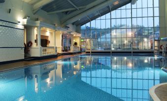 an indoor swimming pool surrounded by a glass wall , with several people enjoying their time in the pool at Village Hotel Liverpool