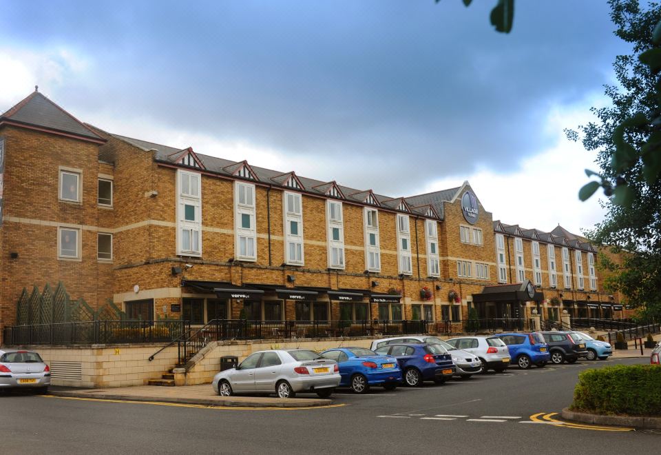 a large brick building with multiple cars parked in front of it , creating a bustling urban environment at Village Hotel Birmingham Dudley