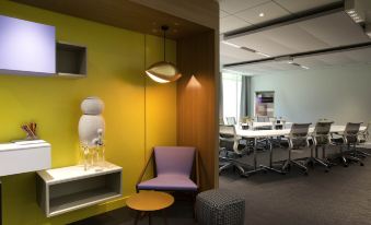 a modern office space with a yellow wall , wooden furniture , and a few people sitting around at Novotel Toulouse Centre Compans Caffarelli