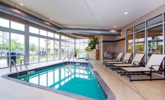 an indoor swimming pool with a curved edge , surrounded by lounge chairs and large windows at Cambria Hotel Appleton