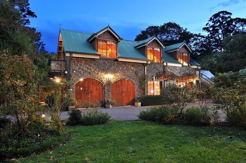 a large stone house with wooden doors and windows , situated in a grassy yard with trees at Mary Cards Coach House