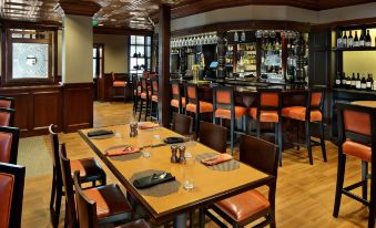 a restaurant with wooden tables and chairs , orange cushions , and a bar area in the background at Gettysburg Hotel