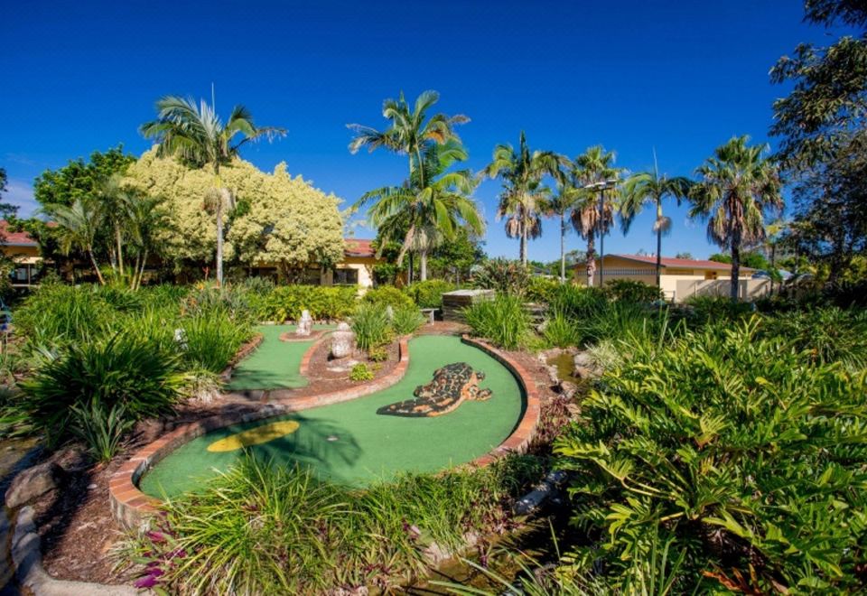 a lush green lawn with a golf course in the background , surrounded by palm trees at Discovery Parks - Ballina
