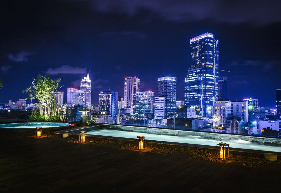 a rooftop patio with a swimming pool surrounded by tall buildings at night , creating a serene atmosphere at Cochin Zen Hotel