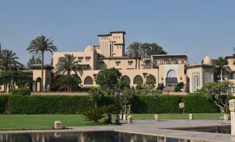 a large building with a swimming pool in front of it , surrounded by palm trees at Marriott Mena House, Cairo