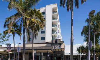 a white building with a blue sign is surrounded by palm trees and other buildings at Rydges Mackay Suites, an EVT hotel