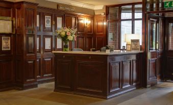 a hotel lobby with a wooden reception desk and chairs , as well as a vase of flowers at Quorn Country Hotel Leicester