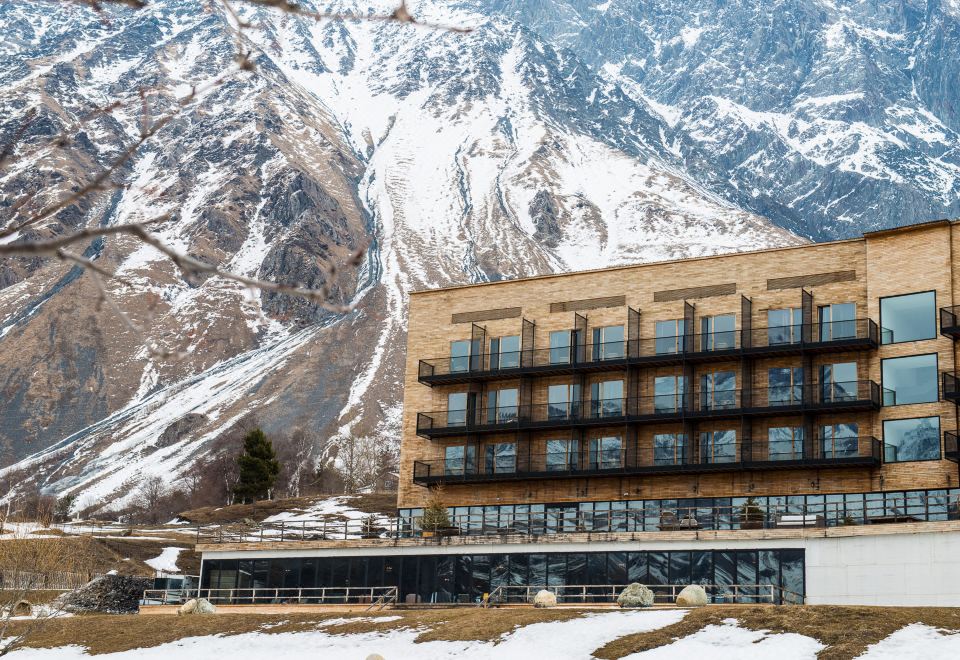 a large , modern building with a wooden exterior is situated in front of a mountain at Rooms Hotel Kazbegi