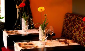 a dining table set for a romantic dinner , with wine glasses , a vase with flowers , and other utensils at Moselhotel & Restaurant Zur Traube Gmbh