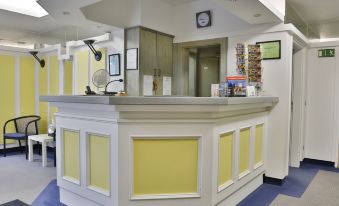 a hotel reception area with a yellow and white counter , a clock on the wall , and various items displayed on the counter at Avenue Hotel