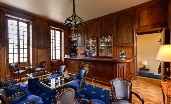 a luxurious living room with wooden paneling , blue carpet , and a bar area with various liquor bottles at Chateau d'Audrieu