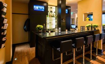 a modern bar with a black counter , black stools , and two tvs on the wall at Hotel Concorde